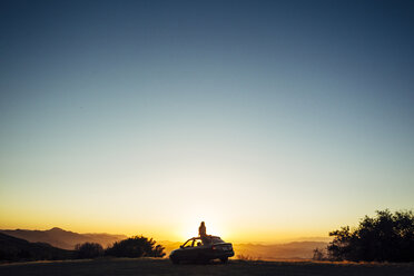 Silhouette Frau sitzt auf dem Autodach gegen den klaren Himmel bei Sonnenuntergang - CAVF62359