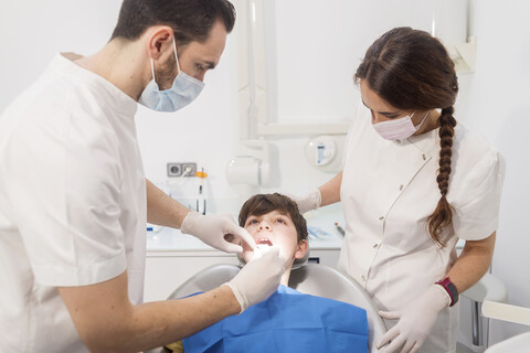 Zahnarzt untersucht die Zähne eines Patienten mit Hilfe einer Assistentin in einer medizinischen Klinik, lizenzfreies Stockfoto