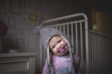 Porträt eines niedlichen Mädchens mit Schnuller im Mund, das zu Hause am Kinderbett steht - CAVF62424