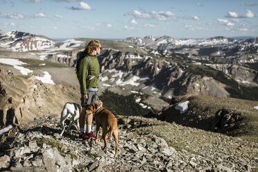 Side view of male hiker with dogs standing on mountain against blue sky during sunny day - CAVF62431