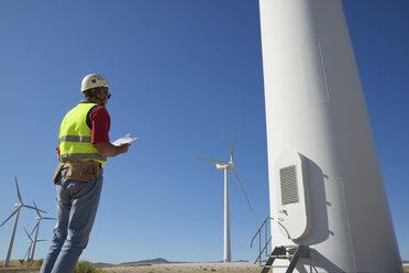 Low angle view of engineer holding clipboard while standing by windmills against sky - CAVF62432