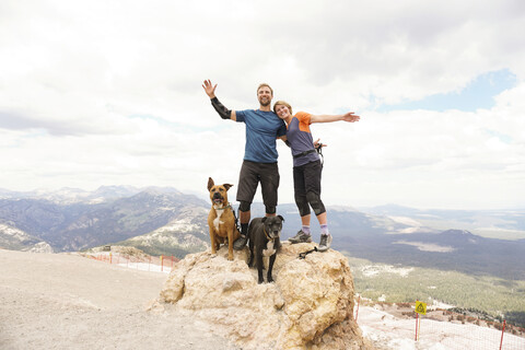 Porträt eines Paares mit Hunden auf einem Berg vor bewölktem Himmel, lizenzfreies Stockfoto