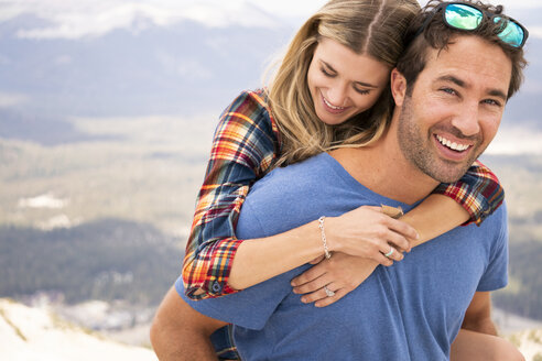 Porträt eines glücklichen Freundes, der seine Freundin huckepack nimmt, während er auf einem Berg steht - CAVF62452