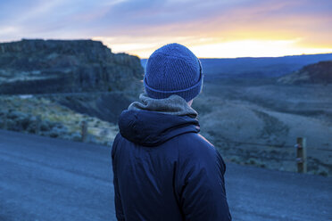 Rear view of woman wearing warm clothing looking at landscape during sunset - CAVF62463