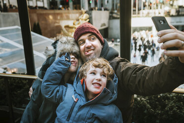 Glücklicher Vater mit Söhnen, die ein Gesicht machen, während sie ein Selfie vor einem Fenster in der Stadt machen - CAVF62465