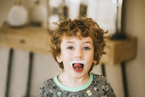 Porträt eines süßen Jungen mit Milchschnurrbart, der zu Hause die Zunge herausstreckt, lizenzfreies Stockfoto