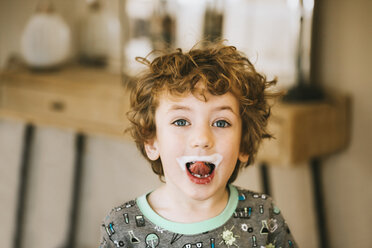 Porträt eines süßen Jungen mit Milchschnurrbart, der zu Hause die Zunge herausstreckt - CAVF62469