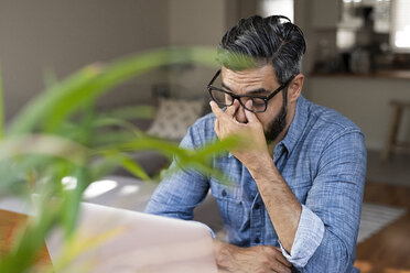 High angle view of stressed businessman with laptop computer sitting at home - CAVF62496