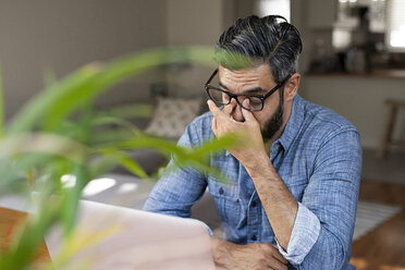 Hoher Blickwinkel auf einen gestressten Geschäftsmann mit Laptop, der zu Hause sitzt - CAVF62496