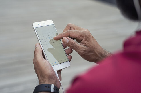 Ausgeschnittenes Bild eines Mannes, der im Freien stehend in den Kalender seines Smartphones schaut - CAVF62503