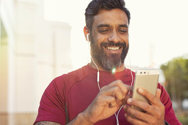 Low angle view of smiling confident man using smart phone while standing against sky - CAVF62504