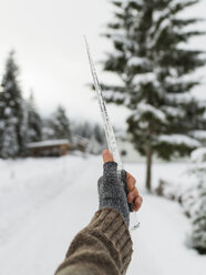 Abgeschnittene Hand einer Frau mit fingerlosem Handschuh, die im Winter einen Eiszapfen hält - CAVF62510