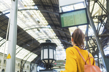 Rückansicht einer Frau mit Rucksack, die am Bahnsteig stehend auf die Abfahrtstafel schaut - CAVF62534