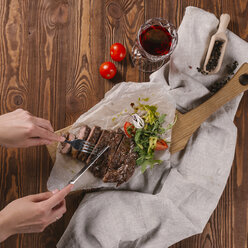 Abgeschnittene Hände einer Frau, die ein Rindersteak mit Besteck auf einem Tisch schneidet - CAVF62542