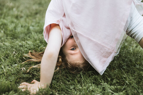 Porträt eines süßen Mädchens, das einen Kopfstand auf einer Wiese im Park übt, lizenzfreies Stockfoto