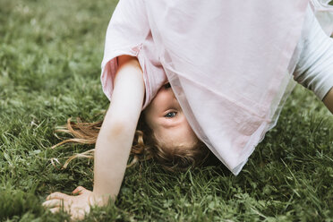 Portrait of cute girl practicing headstand on grassy field in park - CAVF62557