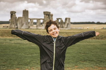 Portrait of smiling boy with arms outstretched standing against old ruins on field - CAVF62559
