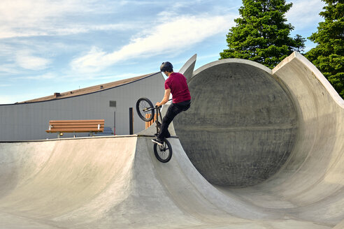 Rückansicht eines Fahrers mit BMX-Rad, der auf einer Betonrampe gegen den Himmel in einem Skateboard-Park springt - CAVF62563