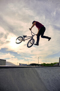 Niedriger Winkel Blick auf männlichen Fahrer mit BMX-Rad Durchführung tailwhip auf Beton Rampe gegen bewölkten Himmel - CAVF62566