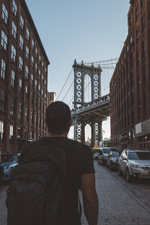Rückansicht eines Mannes mit Rucksack, der auf die Manhattan Bridge blickt, während er auf der Straße steht - CAVF62570