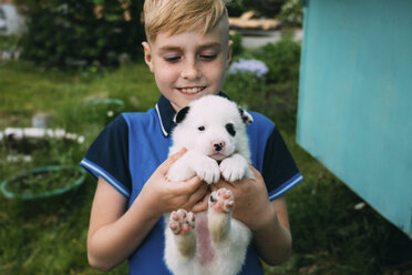 Smiling boy carrying cute puppy while standing in yard - CAVF62591