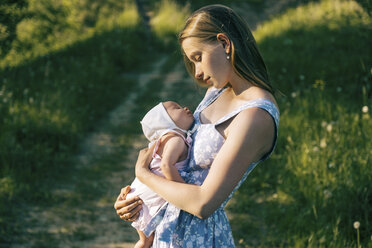 Side view of mother carrying cute newborn daughter while standing on grassy field in park - CAVF62592