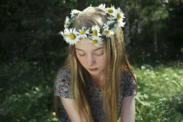 Woman with eyes closed wearing flowers while sitting on grassy field in park - CAVF62596