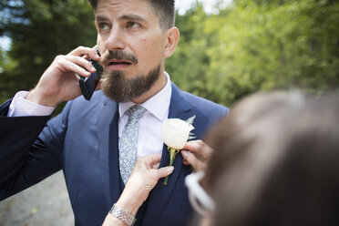 Cropped image of woman adjusting boutonniere on bridegroom's jacket at wedding ceremony - CAVF62599