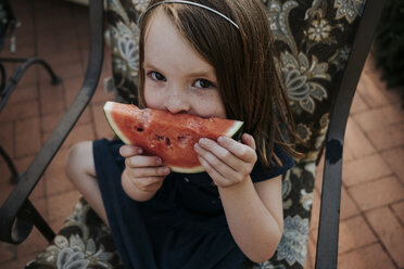 Hohe Winkel Porträt von niedlichen Mädchen essen Wassermelone, während auf Stuhl im Hof sitzen - CAVF62605