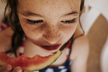 Hochwinklige Nahaufnahme eines nassen Mädchens, das auf einem Stuhl sitzend eine Wassermelone isst - CAVF62609