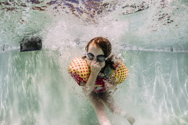 Mädchen mit Schwimmbrille und Schwimmflügeln beim Schwimmen im Pool, das die Nase schließt - CAVF62612