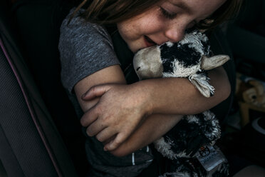 Nahaufnahme eines niedlichen Mädchens, das ein Stofftier umarmt, während es im Auto sitzt - CAVF62614