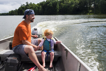 Vater und Sohn genießen eine Fahrt mit dem Motorboot auf einem See im Wald - CAVF62623