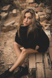 High angle portrait of serious woman sitting on broken bricks at construction site - CAVF62629