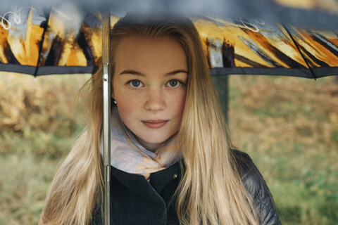 Porträt einer Frau mit blondem Haar, die einen Regenschirm trägt, während sie im Wald steht, lizenzfreies Stockfoto