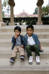 Portrait of cute brothers sitting on steps against sky at Balboa Park - CAVF62642