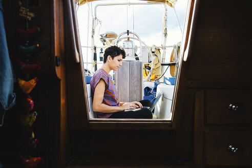 Side view of woman using laptop computer while sitting in boat seen through window - CAVF62653