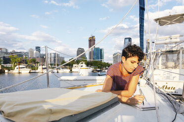 Frau schreibt auf einem Boot liegend gegen den Himmel in der Stadt - CAVF62657