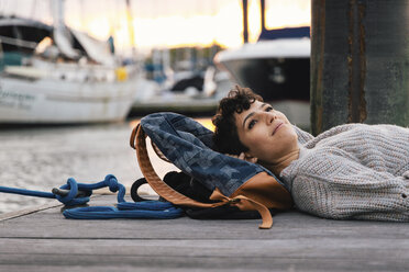 Seitenansicht einer nachdenklichen Frau, die wegschaut, während sie bei Sonnenuntergang auf dem Pier am Hafen liegt - CAVF62665