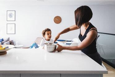 Sohn sieht Mutter bei der Zubereitung von Speisen auf der Kücheninsel zu, während er an der Wand steht - CAVF62667