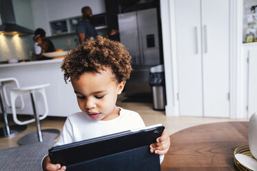 Close-up of cute boy using tablet computer while standing against family at home - CAVF62669