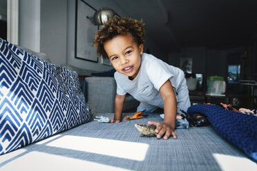 Portrait of cute boy playing with toys on sofa at home - CAVF62671