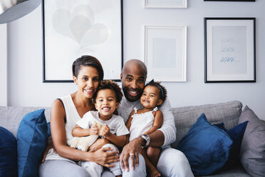 Porträt von lächelnden Eltern mit süßen Kindern, die zu Hause auf dem Sofa sitzen - CAVF62676