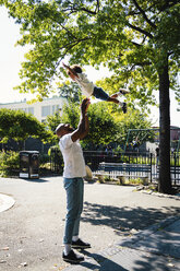 Seitenansicht eines glücklichen Vaters, der seinen Sohn auf dem Fußweg im Park wirft - CAVF62679