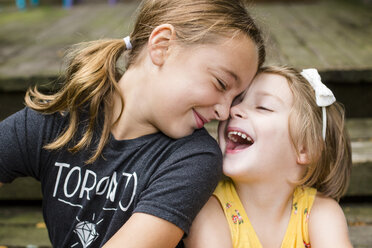 Happy cute sisters looking at each other while sitting on steps in yard - CAVF62690