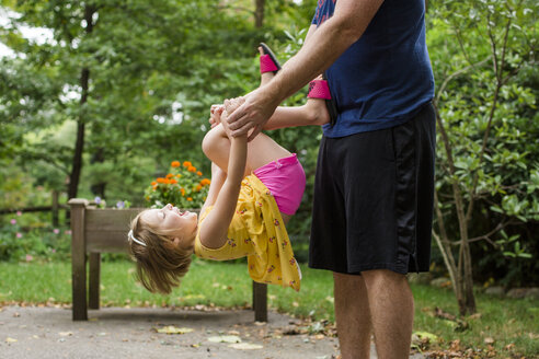 Mittelteil eines verspielten Vaters, der seine niedliche Tochter trägt, während er gegen Bäume im Hof steht - CAVF62691