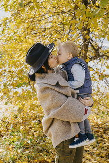 Seitenansicht der Mutter, die ihren Sohn küsst, während sie im Herbst gegen Bäume im Park steht - CAVF62701