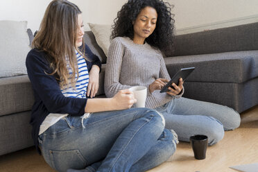 Friends relaxing at home, drinking coffee, using digital tablet - FMOF00427