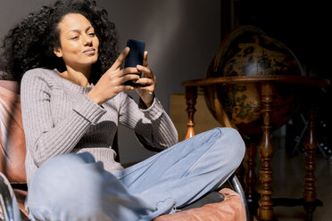 Woman sitting relaxed in armchair, using smartphone - FMOF00451