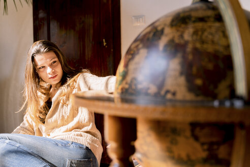 Junge Frau sitzt am Globus und sucht nach Reisezielen - FMOF00452